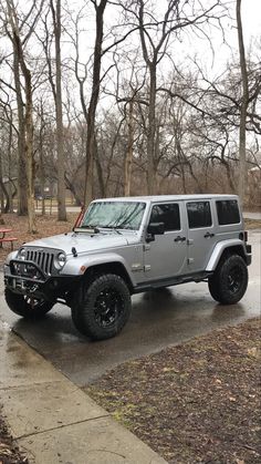 a silver jeep parked on the side of a road next to a park bench and trees