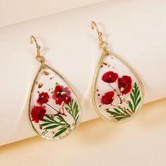 the earrings are decorated with red flowers and green leafy stems on white fabric, hanging from gold - plated earwires