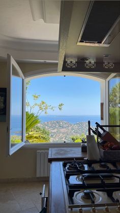 a kitchen with an open window looking out at the ocean and hills in the distance