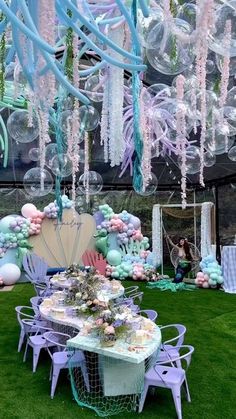 an outdoor party setup with balloons and tables in the grass, under a tented area