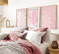 a bed with pink sheets and pillows in a bedroom next to two pictures on the wall