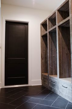 an empty room with wooden shelves and tile flooring in front of a black door