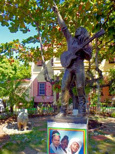 a statue of a man holding a guitar in front of a house with a tree