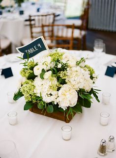 a centerpiece with white flowers and greenery on a table