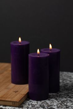 three purple candles sitting on top of a wooden cutting board