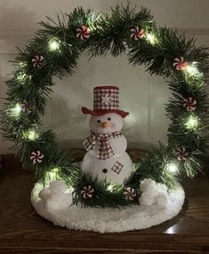 a snowman is sitting in front of a christmas wreath