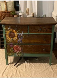 an old dresser with flowers painted on the top and bottom, sitting on a bed