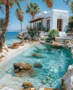 an outdoor swimming pool surrounded by palm trees and water features clear blue waters, whitewashed walls, and steps leading to the beach