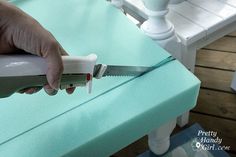 a person is using a knife to cut fabric on a bench with a white chair in the background