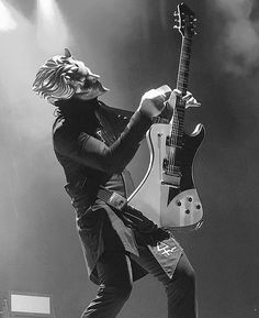 a man with long hair playing an electric guitar in front of a crowd on stage