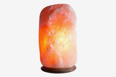 an orange and yellow himalayan salt lamp on a wooden base with a white light behind it