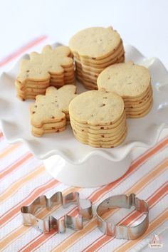 some cookies are on a white plate with cookie cutters next to it and an orange striped table cloth