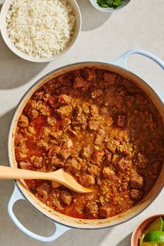 a large pot filled with meat and rice next to bowls full of other food on the table