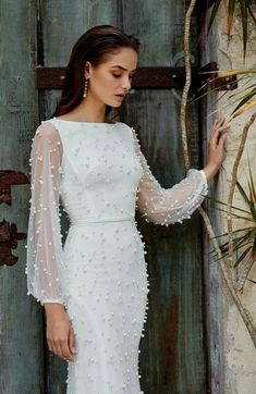 a woman in a white dress standing next to a wooden door with her hand on the wall