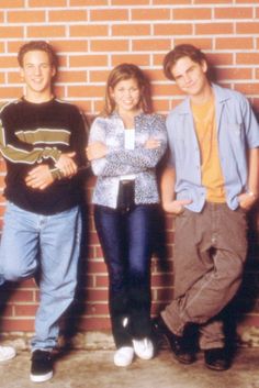 three people standing next to each other in front of a brick wall with their arms crossed