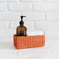 a soap dispenser and hand sanitizer in an orange basket on a white brick wall