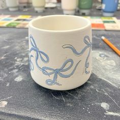 a cup sitting on top of a table next to some paintbrushes and markers