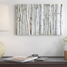 a table with a lamp, vase and painting on the wall behind it that has white birch trees