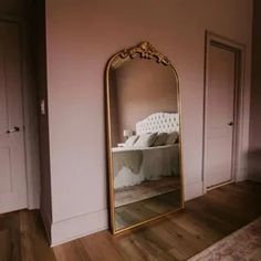 a large gold mirror sitting on top of a wooden floor next to a white bed