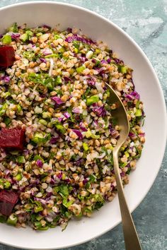 a white bowl filled with rice and veggies next to a fork on top of a table