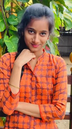 a woman in an orange shirt posing for the camera with her hand on her chin