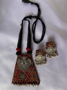 three pieces of jewelry on a white sheet with red and black beads hanging from it's sides