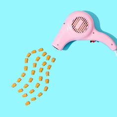 a pink hair dryer with lots of yellow candies coming out of it on a blue background