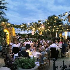 a group of people sitting at tables in a courtyard with string lights strung over them