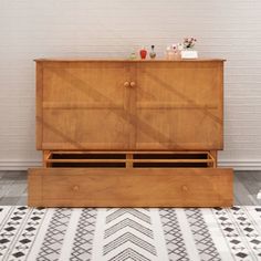 a large wooden cabinet sitting on top of a white and black patterned rug in front of a brick wall