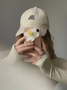 a woman taking a selfie with her cell phone wearing a hat and holding a flower in front of her face