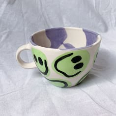 a green and purple cup sitting on top of a white cloth covered table next to a wall