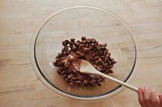 a bowl filled with chocolate chips on top of a wooden table next to a person holding a spoon