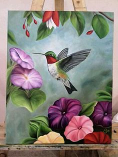 a painting of a hummingbird and flowers on a easel with paintbrushes