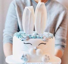 a person holding a cake decorated with white frosting and blue icing, while wearing a bunny ears hat