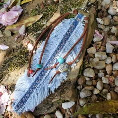 a blue feather and beaded necklace laying on some rocks