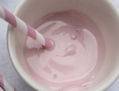 two pink and white striped straws sticking out of a milkshake in a cup