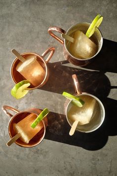 three copper mugs filled with ice and lime slices on top of a cement surface