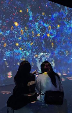 two women sitting in front of a large screen with colorful lights on the wall behind them