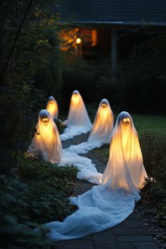 some white ghost statues are lined up in the grass with lights on them and one is glowing