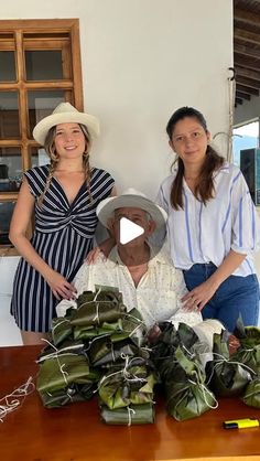 three women standing next to a table with food on it and two are wearing hats