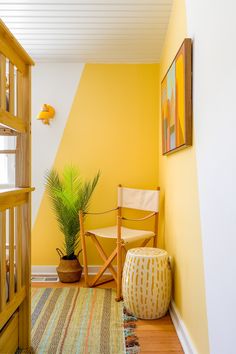 a yellow room with a chair, rug and potted plant