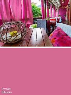 the interior of a restaurant with pink walls and wooden tables, covered by curtains in bright colors