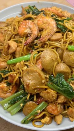 a white plate topped with noodles and shrimp next to green onions on top of a wooden table