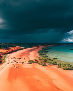 an aerial view of the beach and ocean under a dark sky with storm clouds above