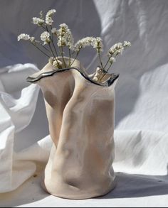 two white vases with flowers in them sitting on a cloth covered tableclothed surface