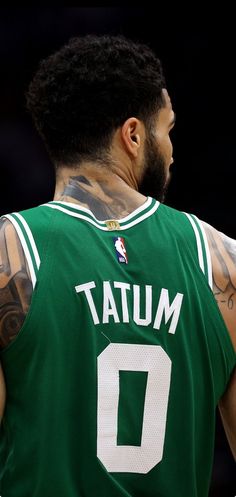 the back of a basketball player with tattoos on his arms and shoulder, wearing a green jersey