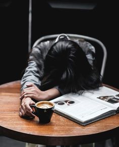 a person sleeping on top of a wooden table next to a cup of coffee