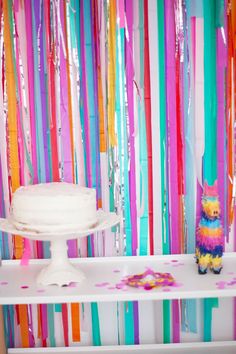 a cake on a table in front of colorful streamers and a small stuffed animal