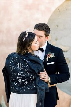 a man in a tuxedo hugging a woman who is wearing a jacket with writing on it