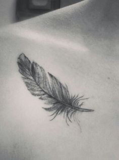 a black and white photo of a woman's chest with a feather tattoo on it